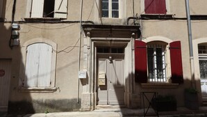 A building with a central entrance, a small balcony, and a window with red shutters.