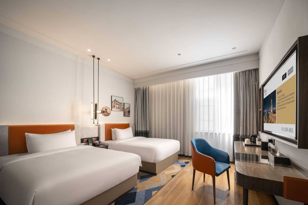 Ett hotellrum med två sängar, ett skrivbord, en stol och en TV.