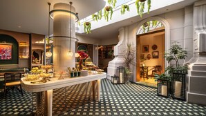Een ruime hotel lobby met een bar in het midden, hangplanten en een vloer met een patroon.