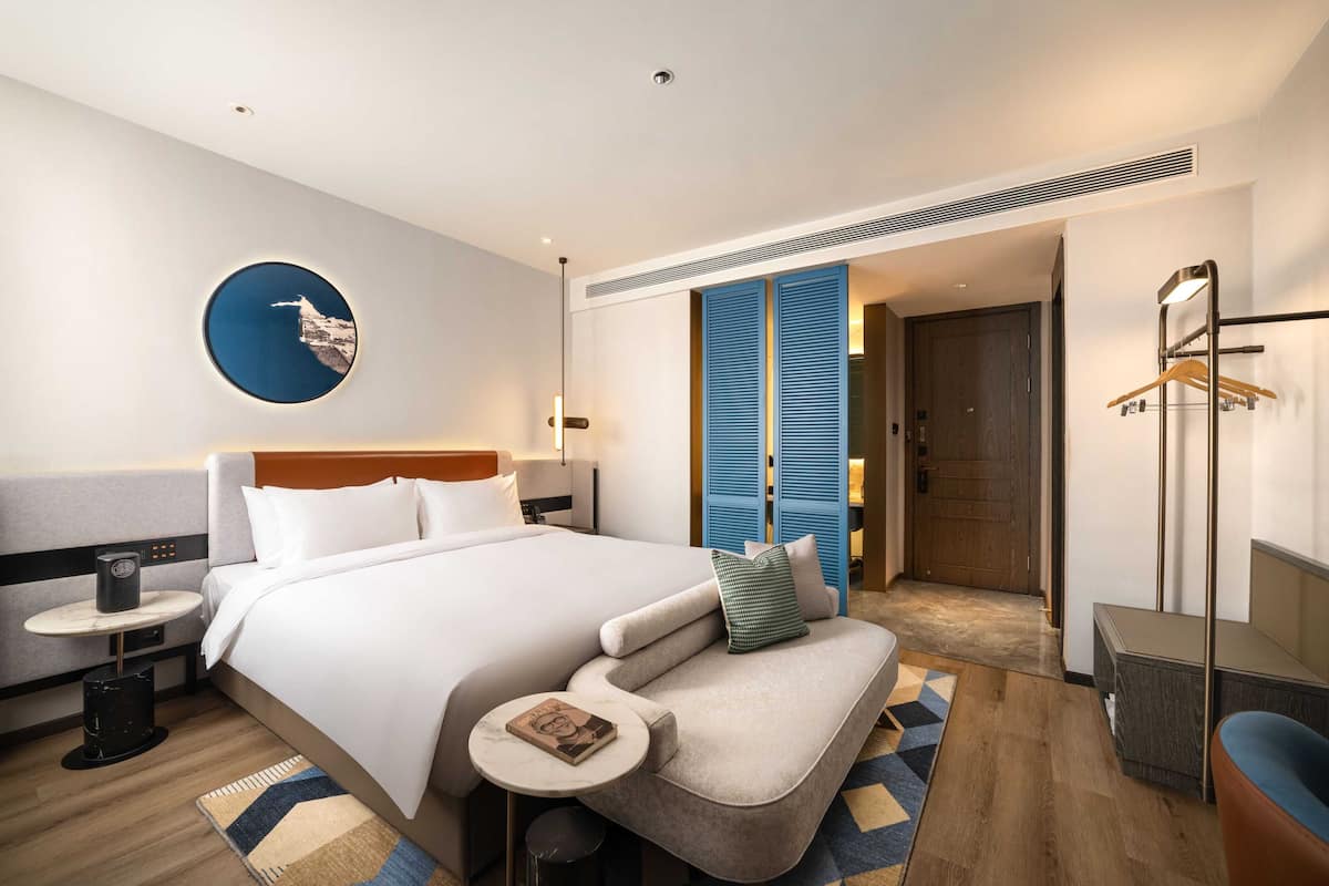 Ett modernt hotellrum med en stor säng, en sittgrupp, ett litet bord och en garderob.