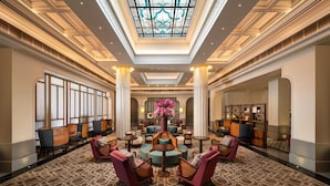 Een ruime lobby met een hoge plafond, een kamerbreed tapijt met patroon, en een centraal zitgedeelte met stoelen en tafels.