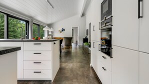 A modern kitchen with white cabinetry, a large island with a sink, and a view of the outdoors through large windows.