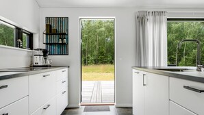 A modern kitchen with white cabinetry, a coffee machine, and a view of a deck and forest.