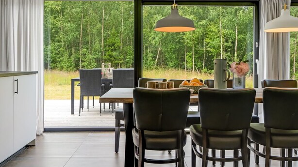 A dining area with a table and chairs, large windows with a forest view, and pendant lighting.