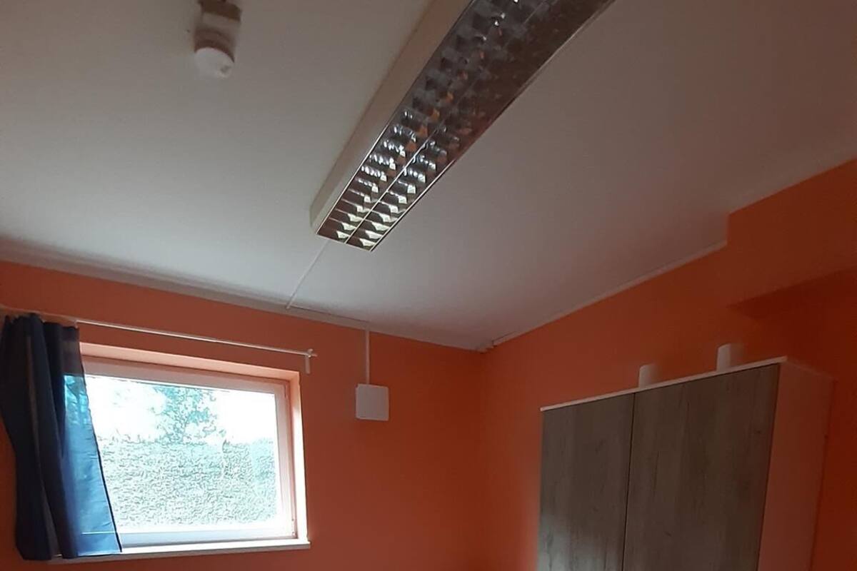 Een kleine, lichte kamer met oranje wanden, een houten vloer, een enkel bed, een bureau en een kledingkast.