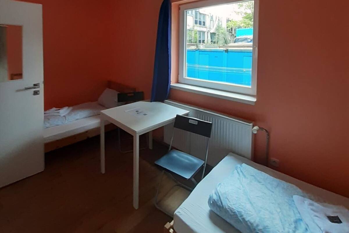 Een kleine kamer met twee enkele bedden, een wit bureau en een raam met uitzicht op een zwembad.