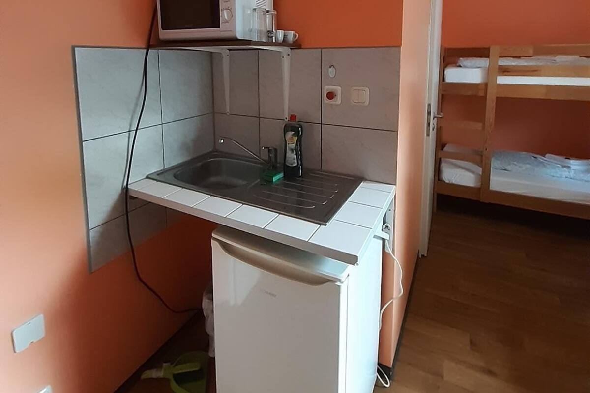 Een compacte keuken met een magnetron, spoelbak en kleine koelkast. Een stapelbed is zichtbaar in de aangrenzende kamer.
