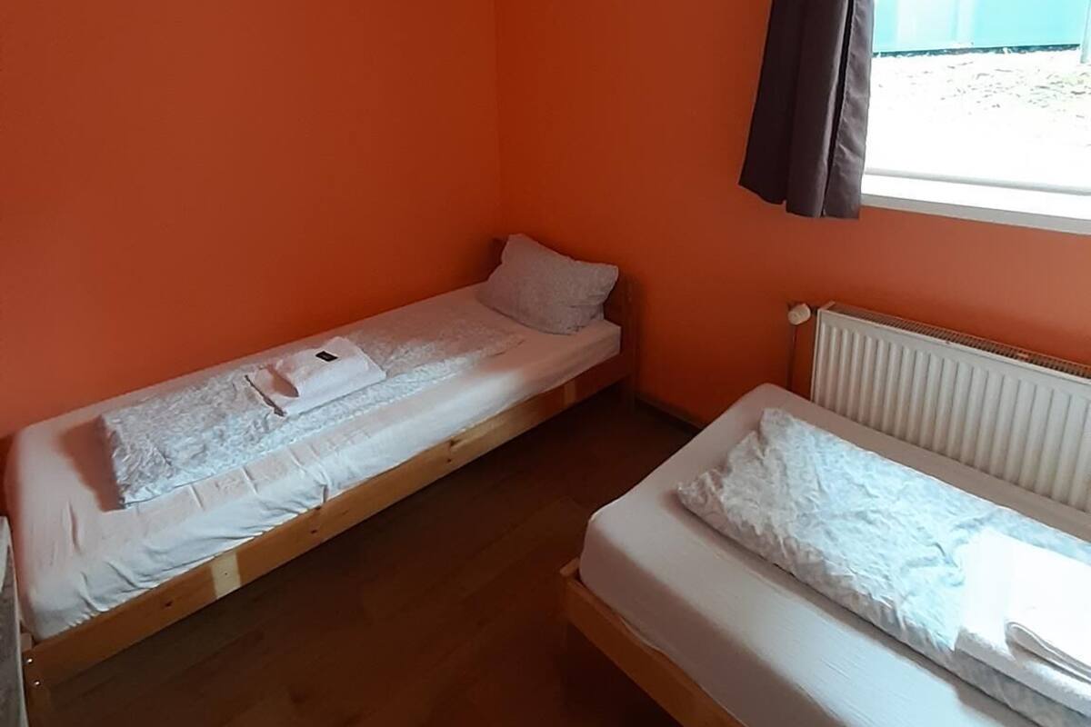Een kleine kamer met twee eenpersoonsbedden, oranje wanden, een raam met gordijnen en een radiator.