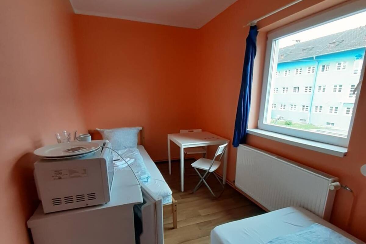 Een kleine kamer met oranje wanden, een bed, een bureau en een radiator.