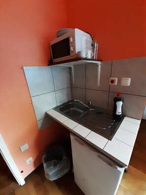 Eine kleine Küche mit Spüle, Mikrowelle und einem Kühlschrank.