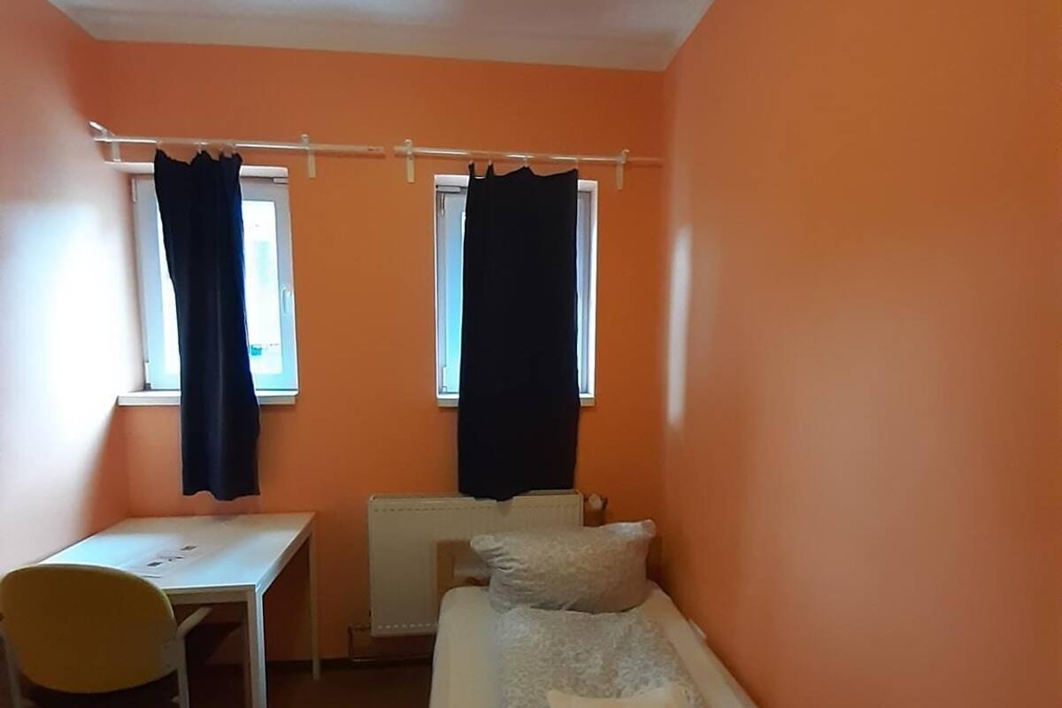 Een kleine, eenvoudige accommodatie met een bed, een tafel en een stoel.