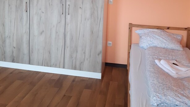 A bedroom with a wooden wardrobe, a bed with a patterned duvet, and a wooden floor. - 2-Rent Group Hostel Rooms&Apartments TUB19A (Munich)