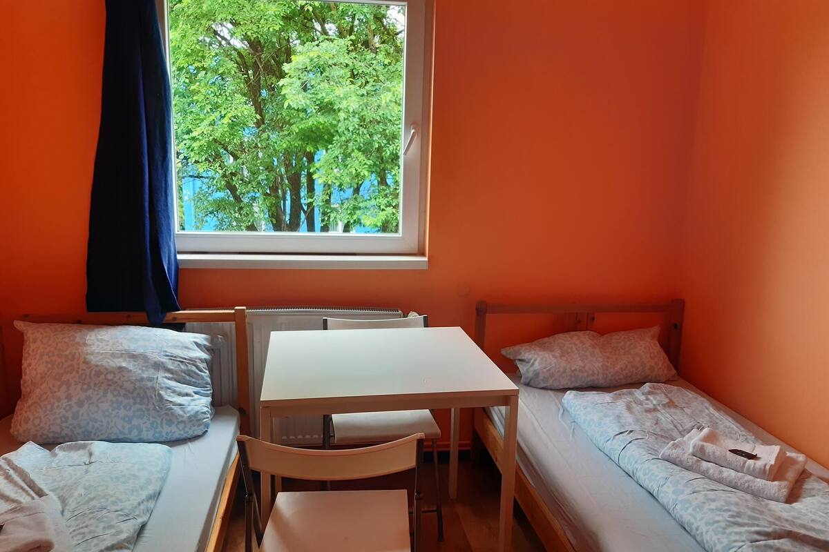 Una habitación pequeña con dos camas individuales, una mesa de madera y una silla.