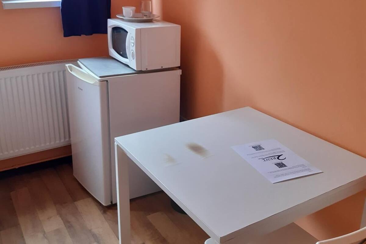 Una pequeña cocina americana equipada con microondas, un refrigerador compacto y una mesa con una silla.