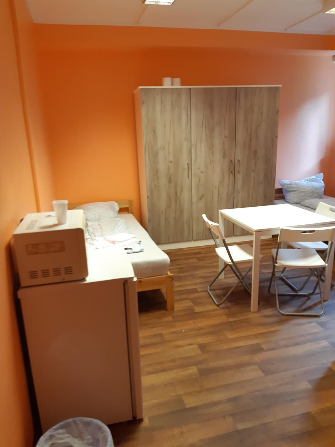 Una habitación compacta con un armario de madera, una mesita con sillas, una cama y un calentador portátil.