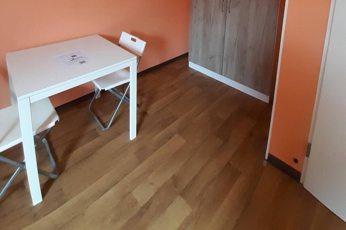 Een kamer met een witte tafel en stoelen, een houten garderobe en oranje wanden.