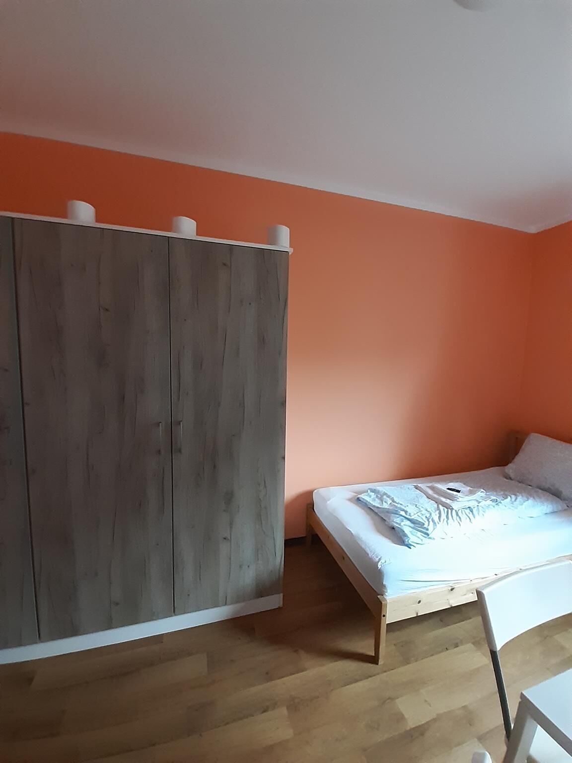 Ein Schlafzimmer mit einem Holzschrank, einem Bett mit weißer Bettwäsche und einer orangefarbenen Wand.