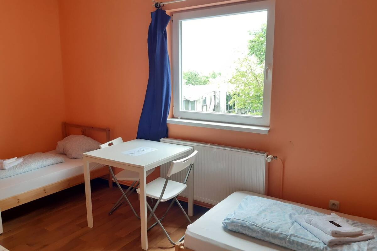 Una habitación pequeña con paredes anaranjadas, dos camas individuales, una mesa y una silla.
