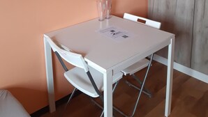 Un petit coin repas avec une table et des chaises blanches, une armoire en bois et un mur de couleur pêche.