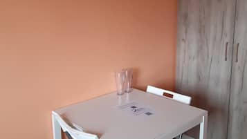 Ein kleiner Essbereich mit einem weißen Tisch und Stühlen, einem Holzschrank und einer pfirsichfarbenen Wand.