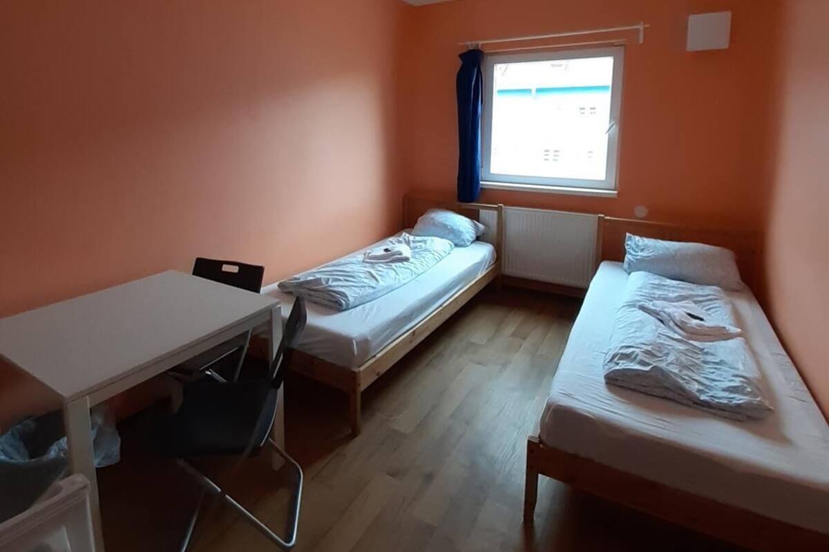 Een kleine kamer met oranje wanden, twee eenpersoonsbedden, een bureau en een stoel.