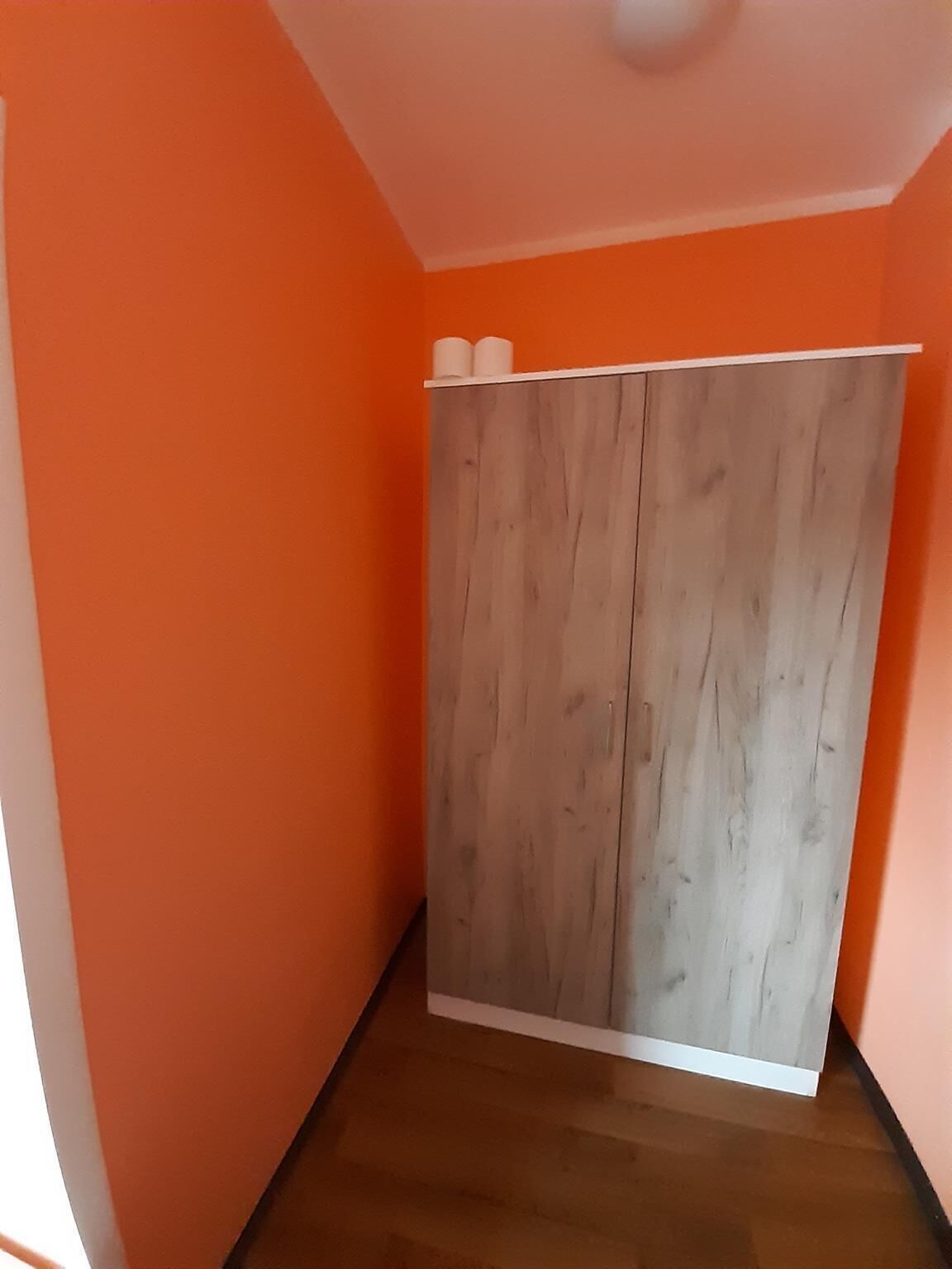 A room with orange walls, a wooden wardrobe, and a brown floor.