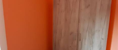 A room with orange walls, a wooden wardrobe, and a brown floor.