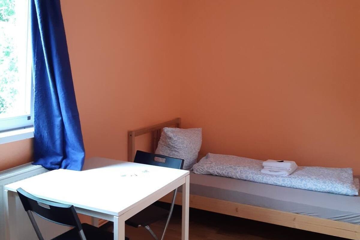 Een kleine kamer met een enkel bed, een tafel en een stoel.