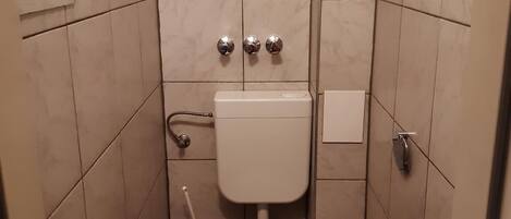 Une petite salle de bain comprenant des toilettes, un lavabo et deux robinets d’évacuation fixés au mur.