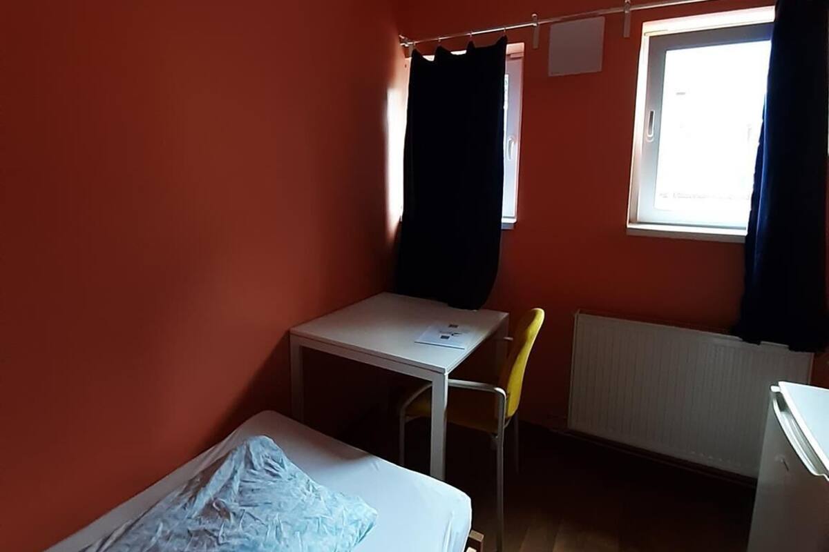 Een kleine, eenvoudige kamer met een bed, een bureau en een stoel.