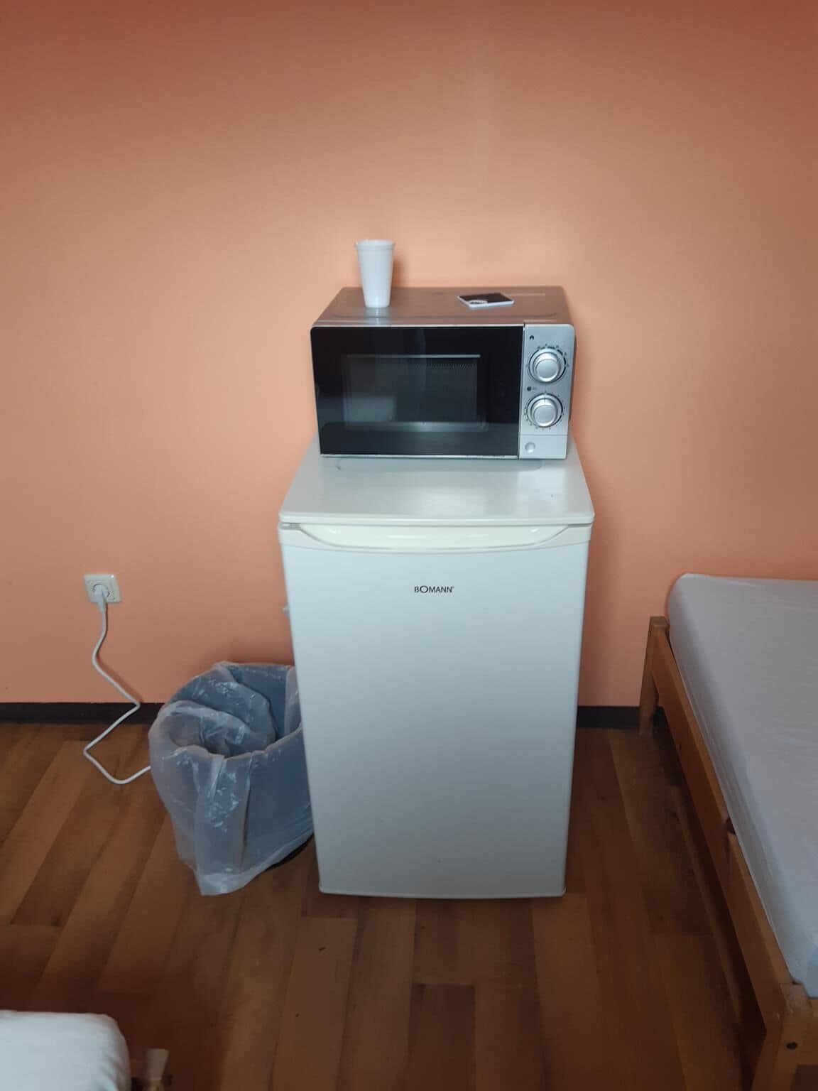 Une petite cuisine équipée, avec un micro-ondes posé sur un petit réfrigérateur, une prise de courant et un plancher en bois.