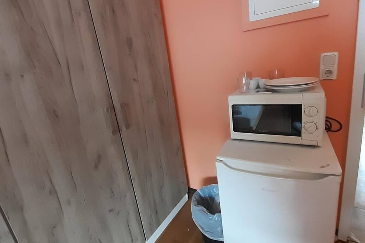 Een compact keuken met een magnetron, een kleine koelkast en een houten garderobe.