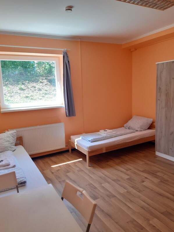 A small, single-bed room with a wooden floor, a window with a view of greenery, and a radiator. - 2-Rent Group Hostel Rooms&Apartments TUB19A (Munich)