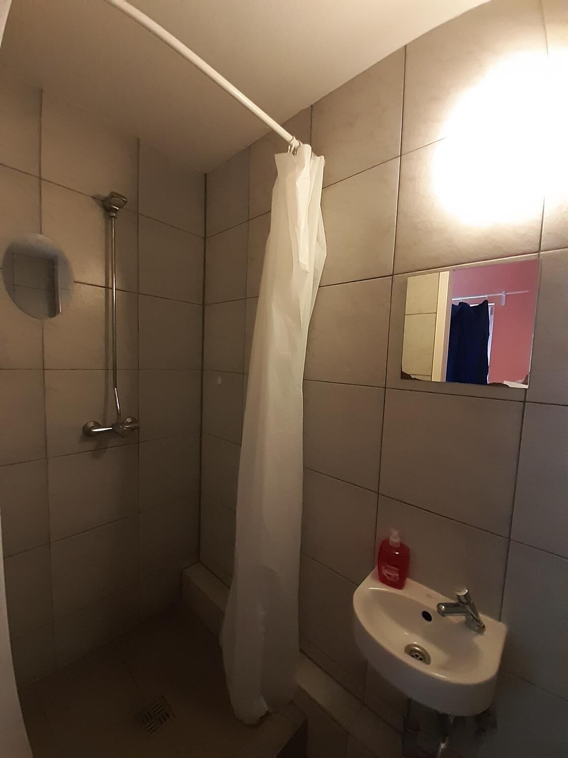 Un baño con ducha, lavamanos y espejo.