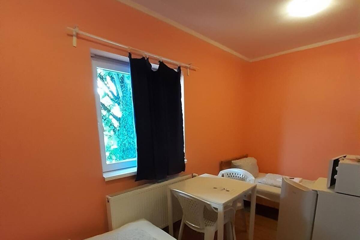 Een kleine, compacte kamer met een bed, een bureau, een stoel en een koelkast.