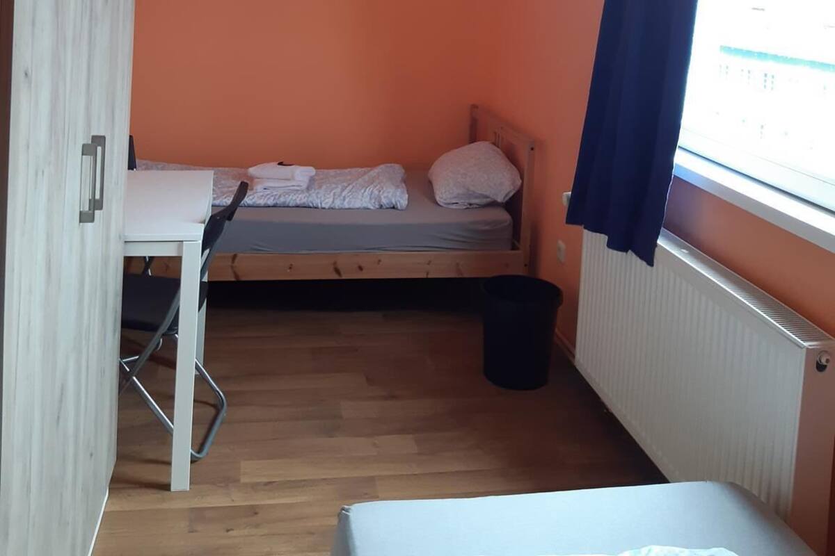 Una habitación pequeña con pared naranja, una cama de madera, un escritorio y una ventana con cortina.