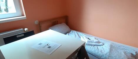 Una habitación pequeña con una cama, un escritorio y una silla. Hay una ventana en un lateral.
