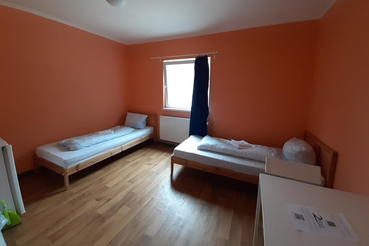 Une chambre avec deux lits simples, un plancher en bois, une fenêtre avec un rideau et un radiateur.