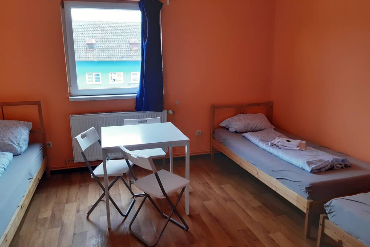 Un dormitorio con dos camas individuales, una mesita con sillas y una ventana con cortinas.