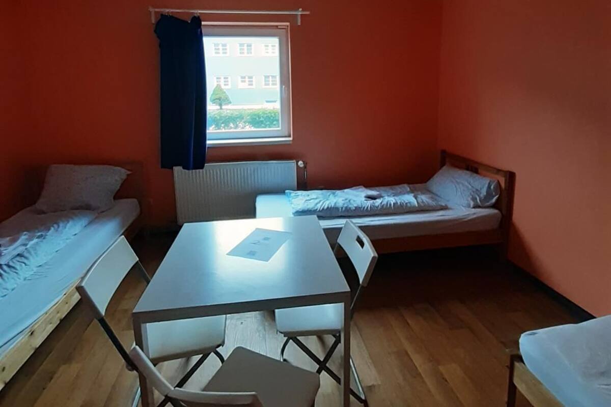 Een studentenkamer met twee eenpersoonsbedden, een klein tafeltje en een stoel.