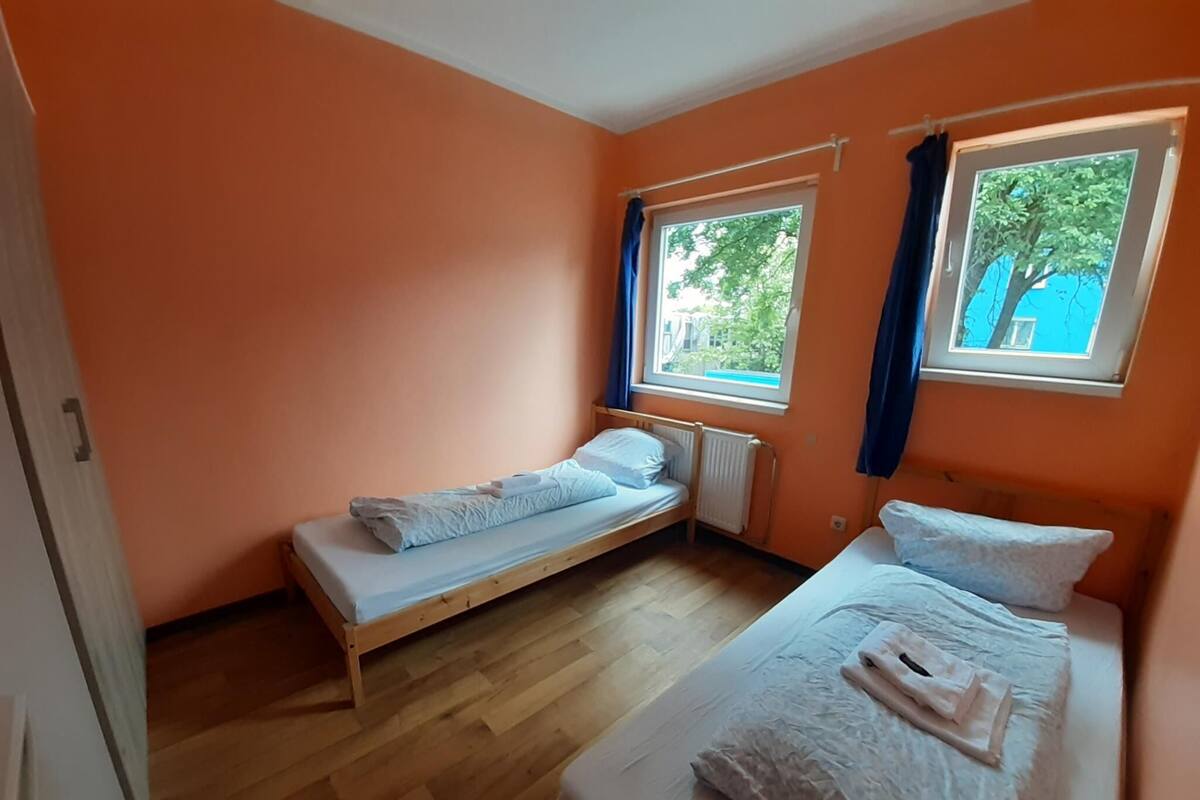 Een klein appartement met één kamer, twee bedden, houten vloeren en ramen met gordijnen.