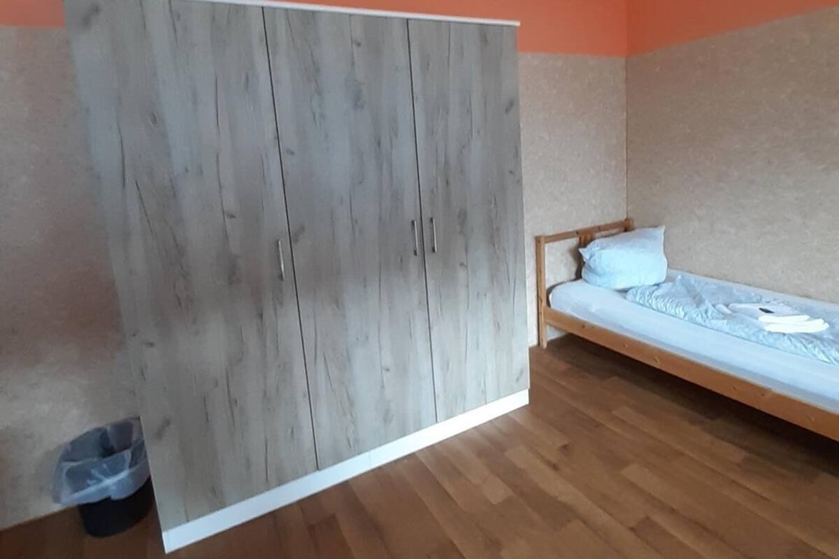 Een slaapkamer met een houten garderobe, een bed met een wit matras, en oranje wanden.