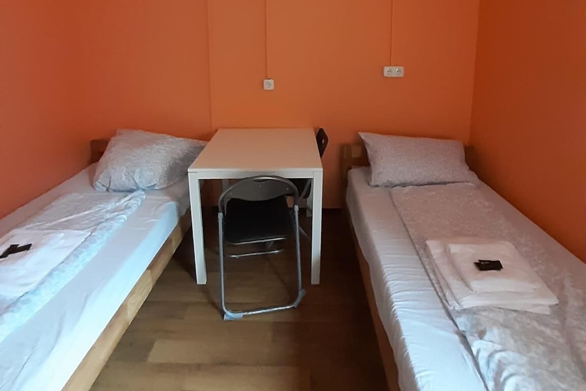 Une petite pièce avec deux lits simples, une petite table et une chaise.