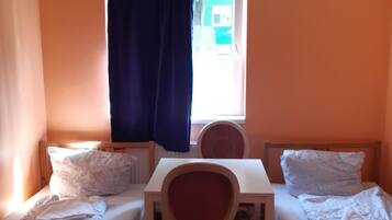 A small room with two single beds, a wooden table, and a chair.