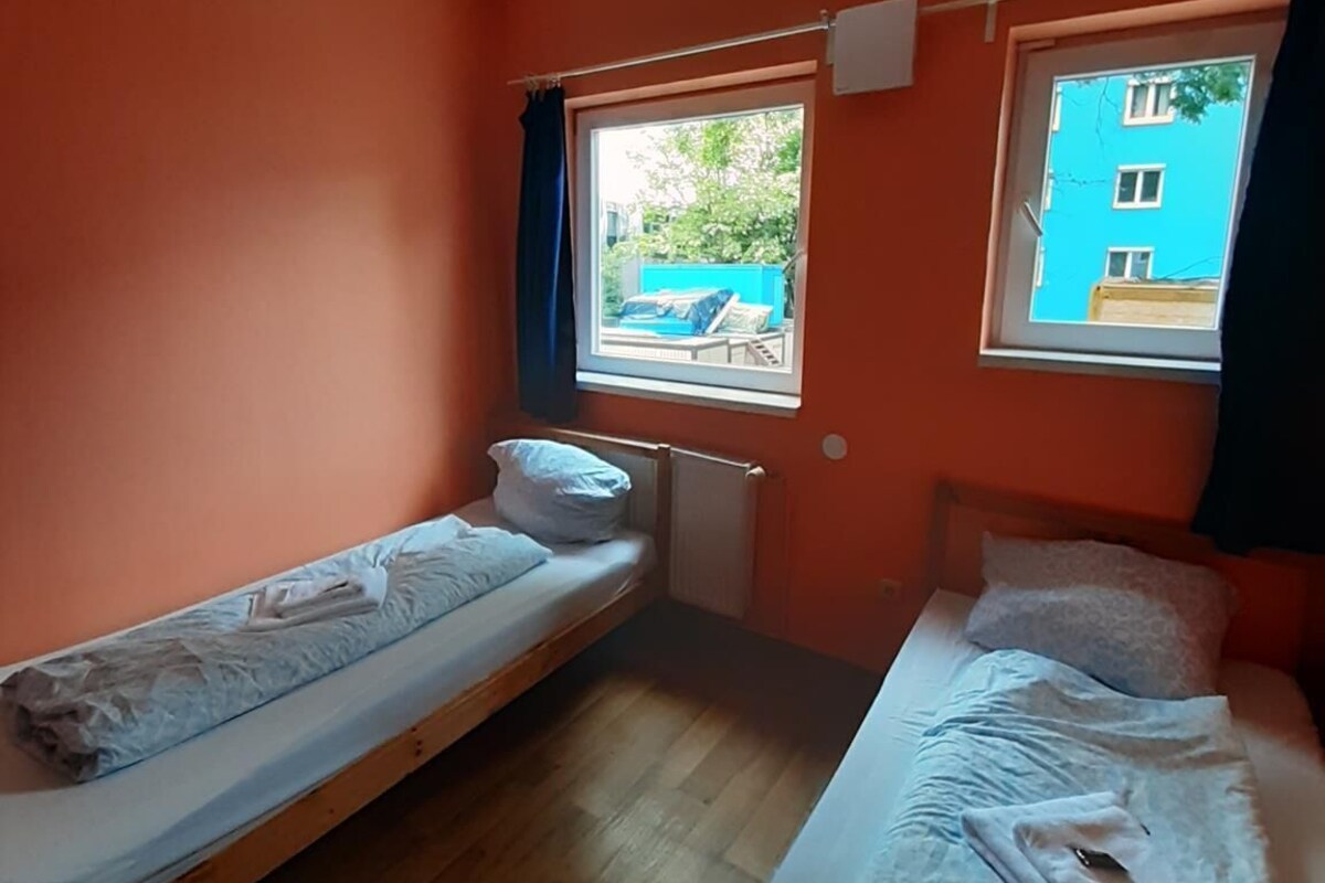 Ein kleines Zimmer mit zwei Betten, einem Fenster und Blick auf ein Gebäude.