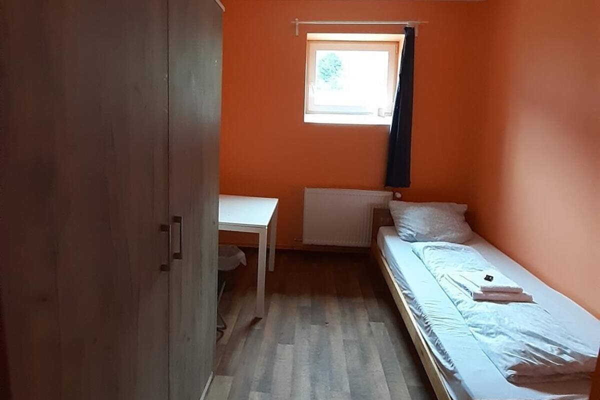 Een klein appartement met één kamer, een houten kast, een tafeltje, een bed en een radiator.