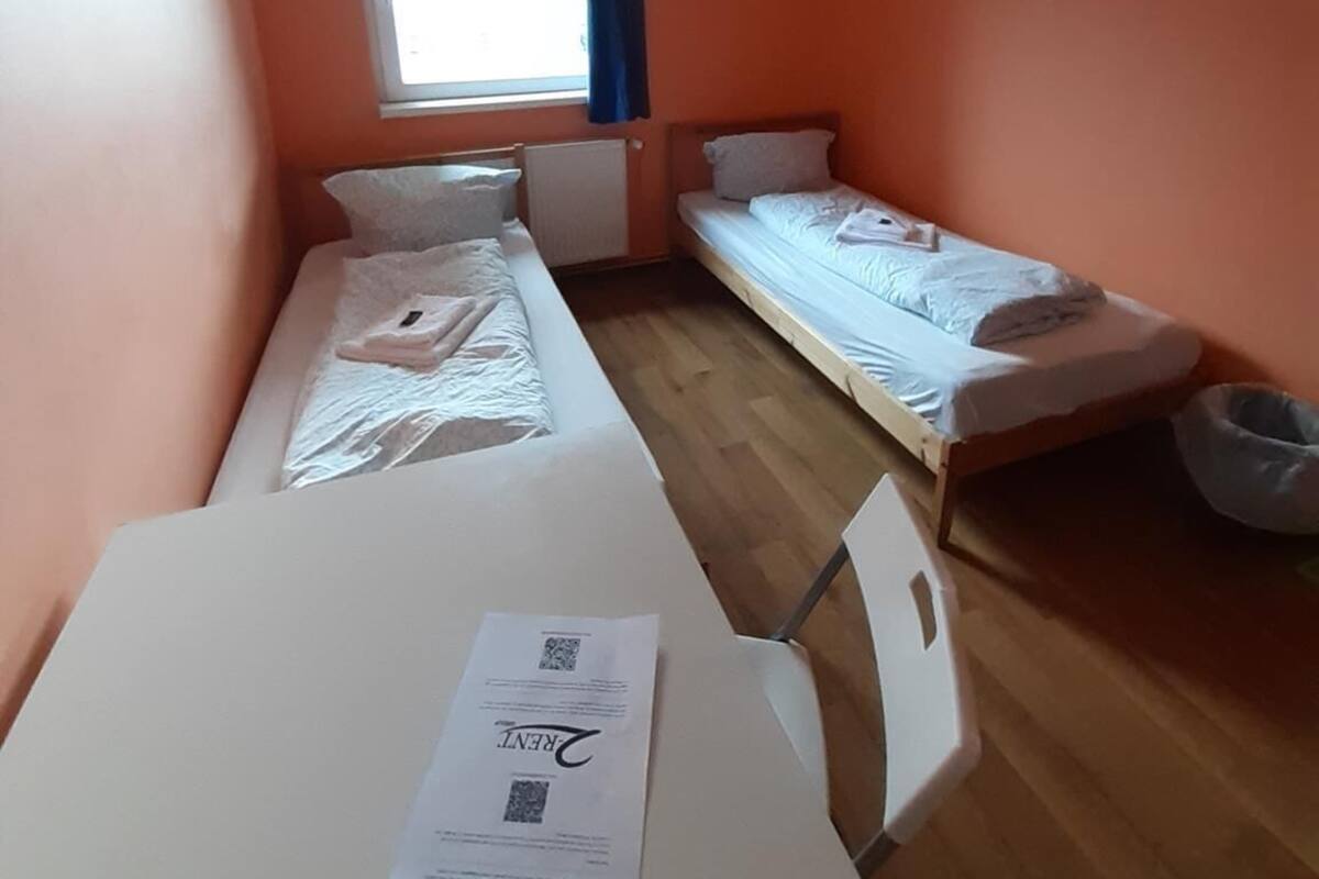 Een kleine kamer met twee eenpersoonsbedden, een tafel met een stoel en een raam met gordijnen.