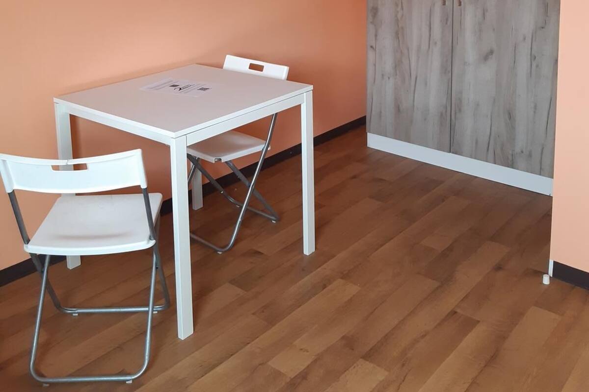 Una habitación con una mesa y sillas blancas, paredes anaranjadas y un armario de madera.