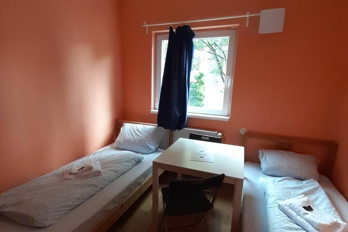 Een kleine kamer met twee eenpersoonsbedden, een tafel en een raam met gordijnen.