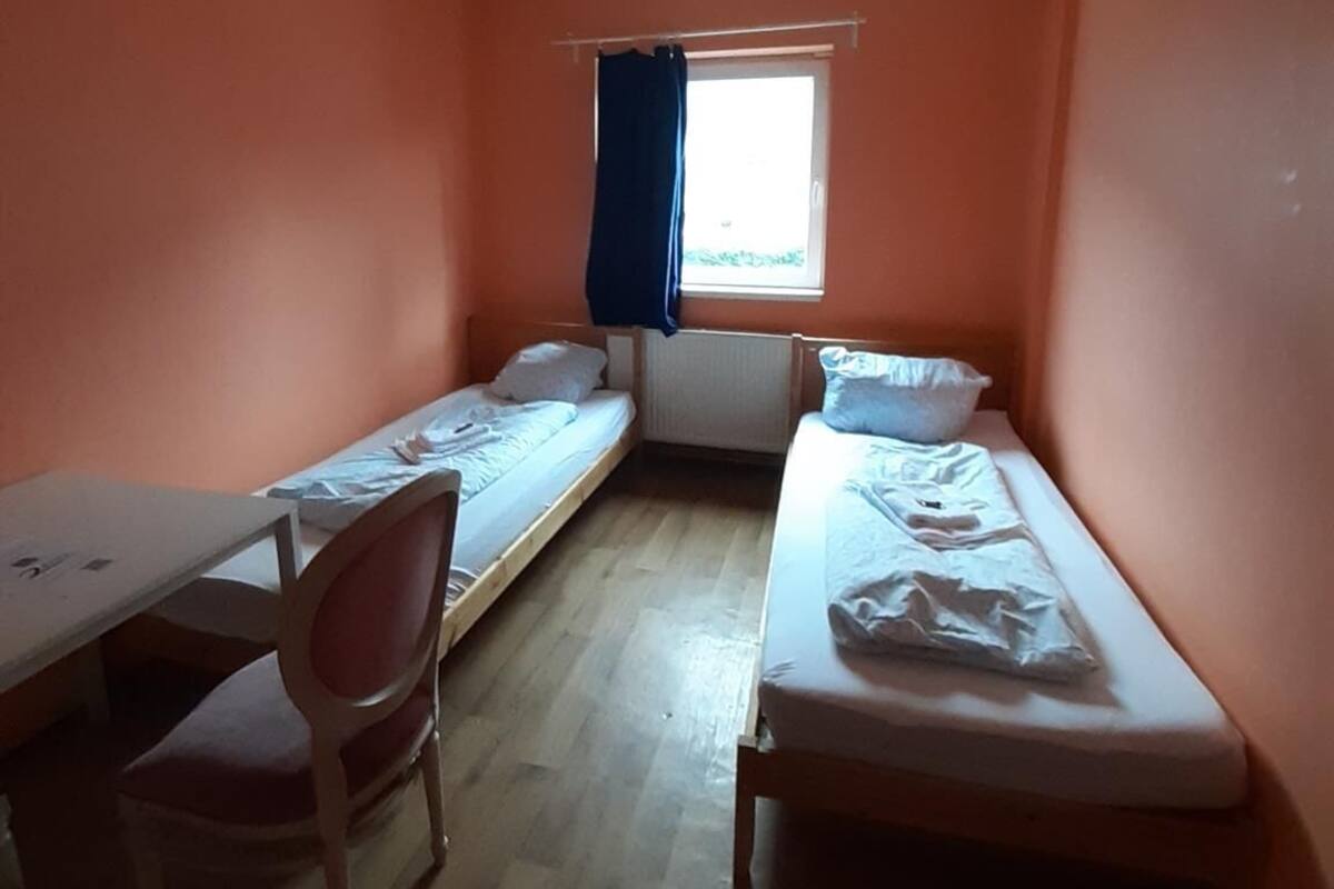 Een studentenkamer met twee eenpersoonsbedden, een bureau en een stoel.